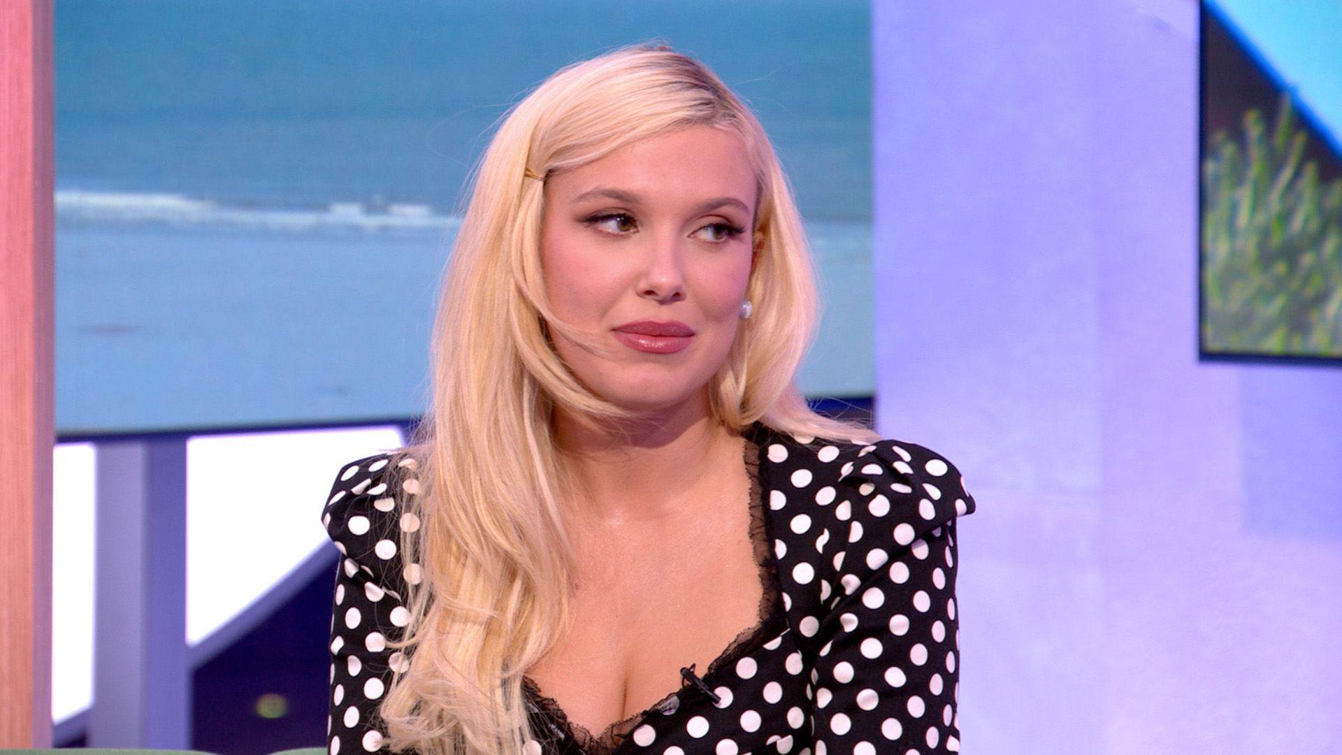 Millie Bobby Brown wearing a black and white dotted dress sitting on the green The One Show sofa