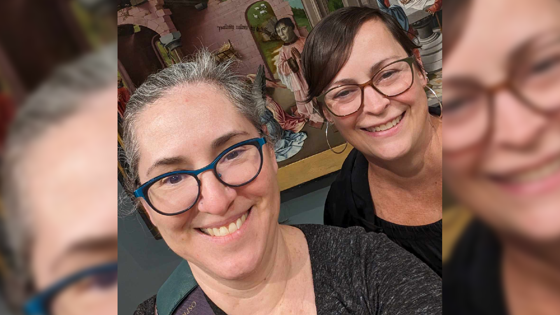 Two women stand in front of a painting.