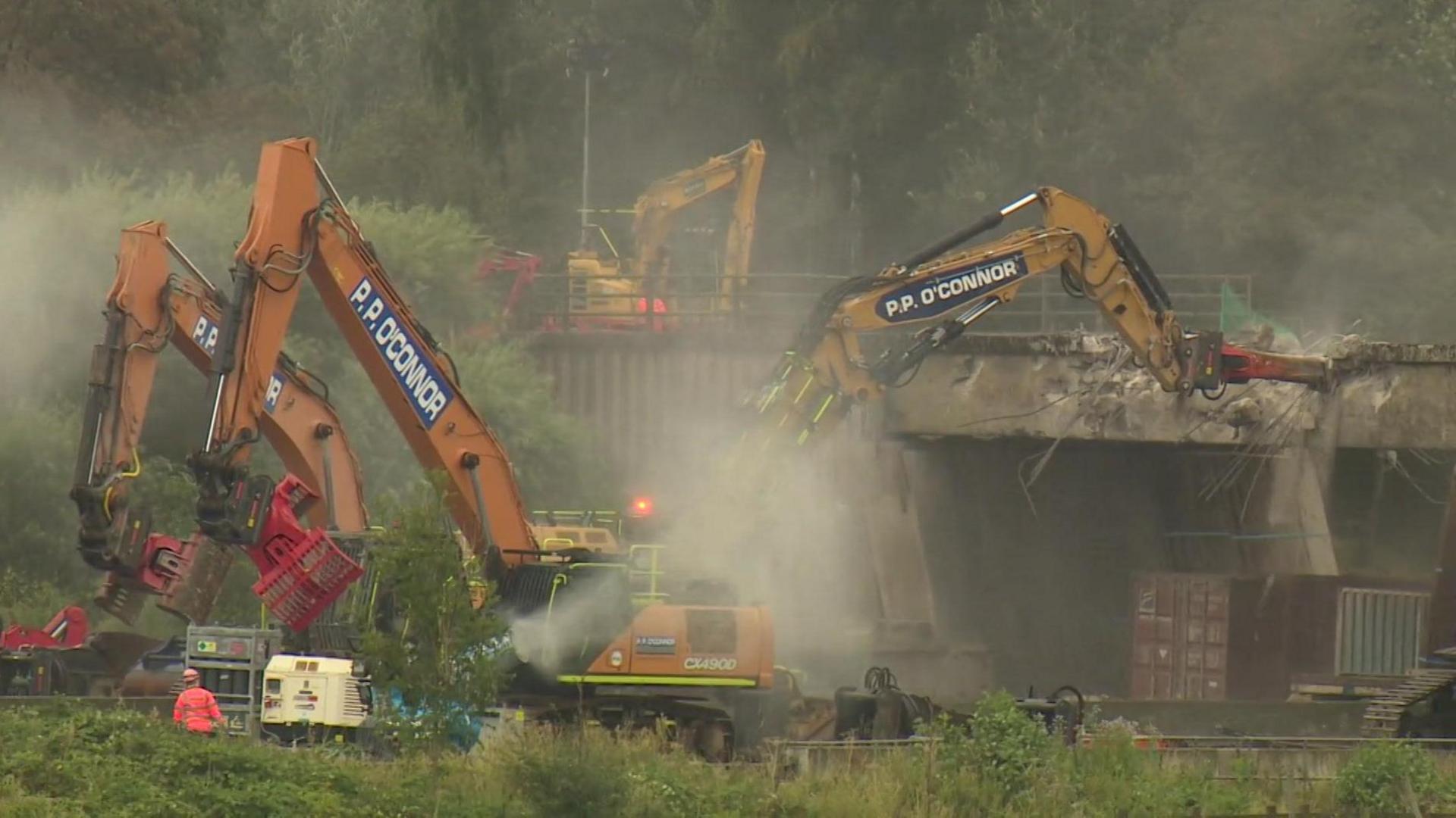 A bulldozers crashes into the bridge as it demolishes it