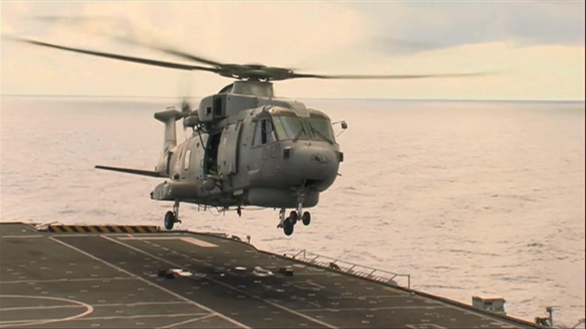 A helicopter carries hovers over HMS Illustrious' flight deck