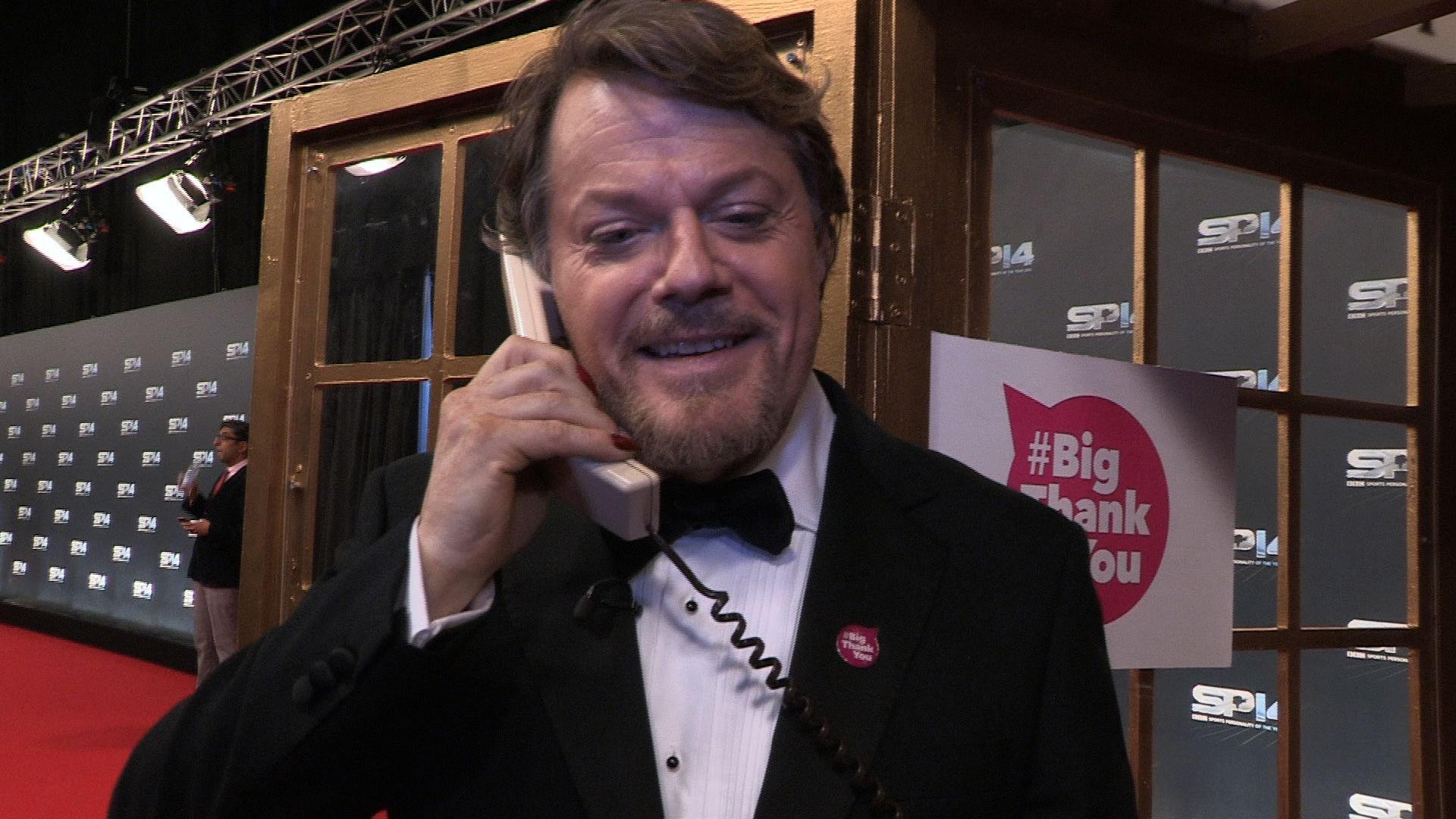 Eddie Izzard standing outside a phone box on the telephone