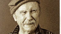 A black and white phot of Padraic Fiacc. He has a moustache and is wearing a woollen cap and a striped shirt.