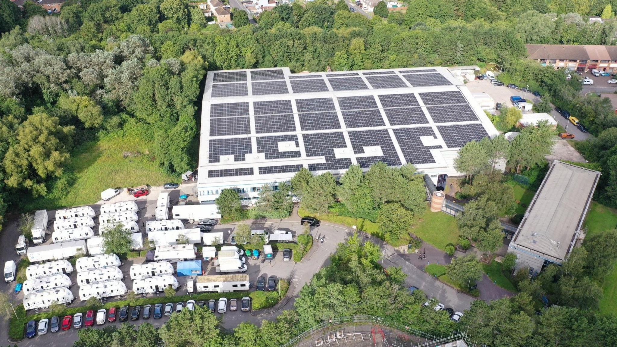 An aerial view of The Bottle Yard Studios which has solar panels all over the roof and about 15 white production trailers to the left of it