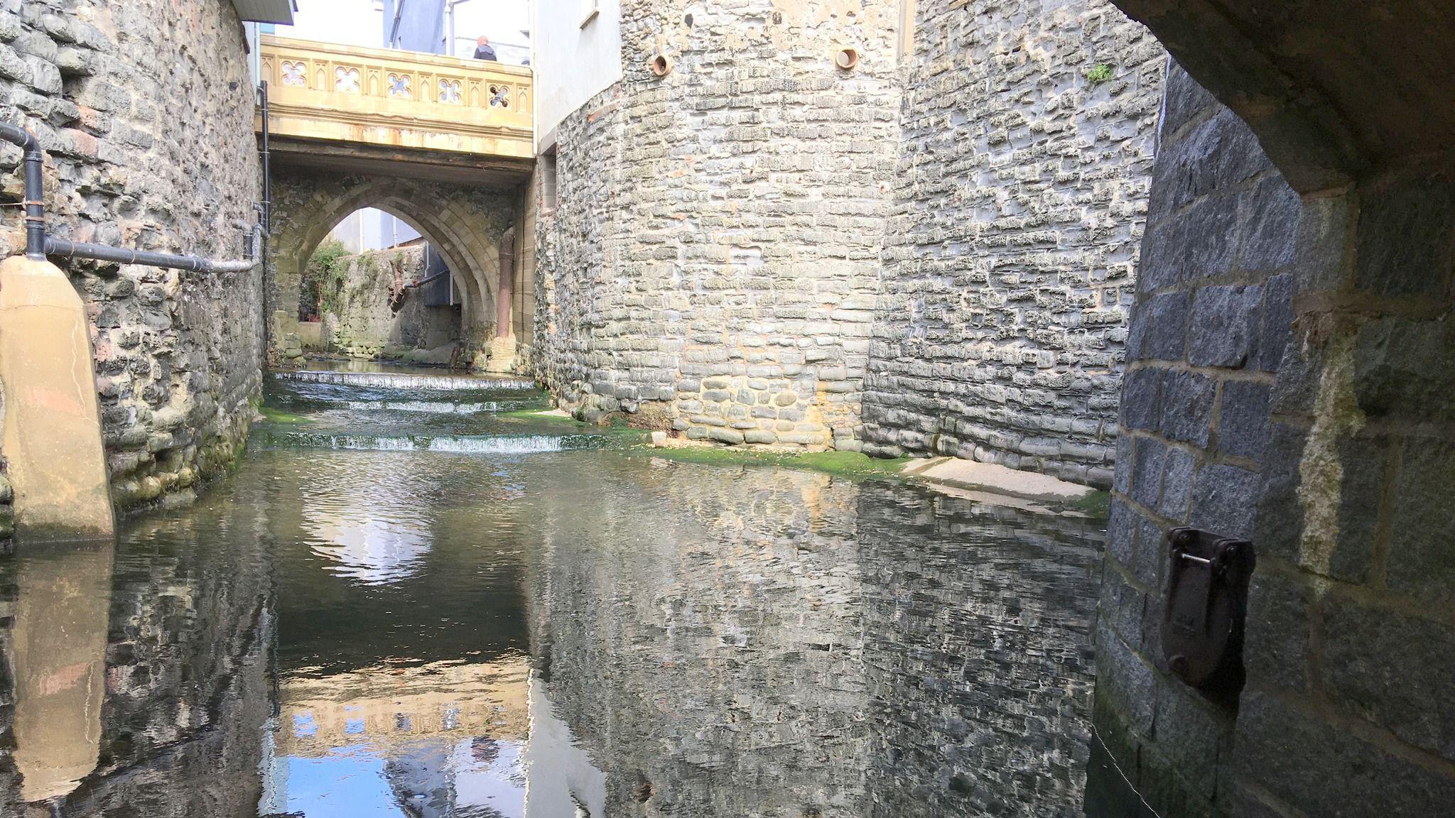 The River Lim viewed from beneath a stone bridge. The view is far below street level and the river is running through a deep channel with high stone walls either side.