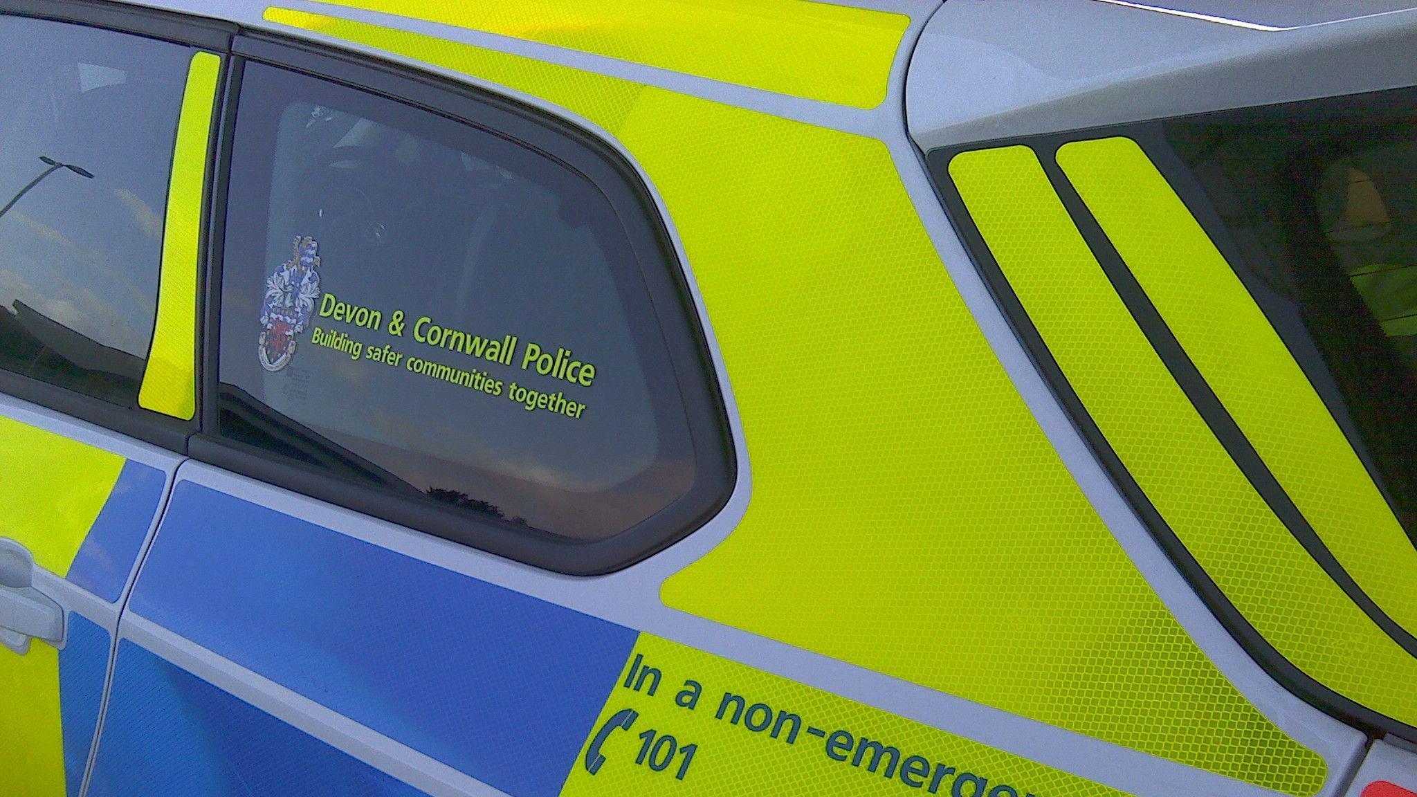 The side of a Devon & Cornwall police car painted yellow and blue and white.