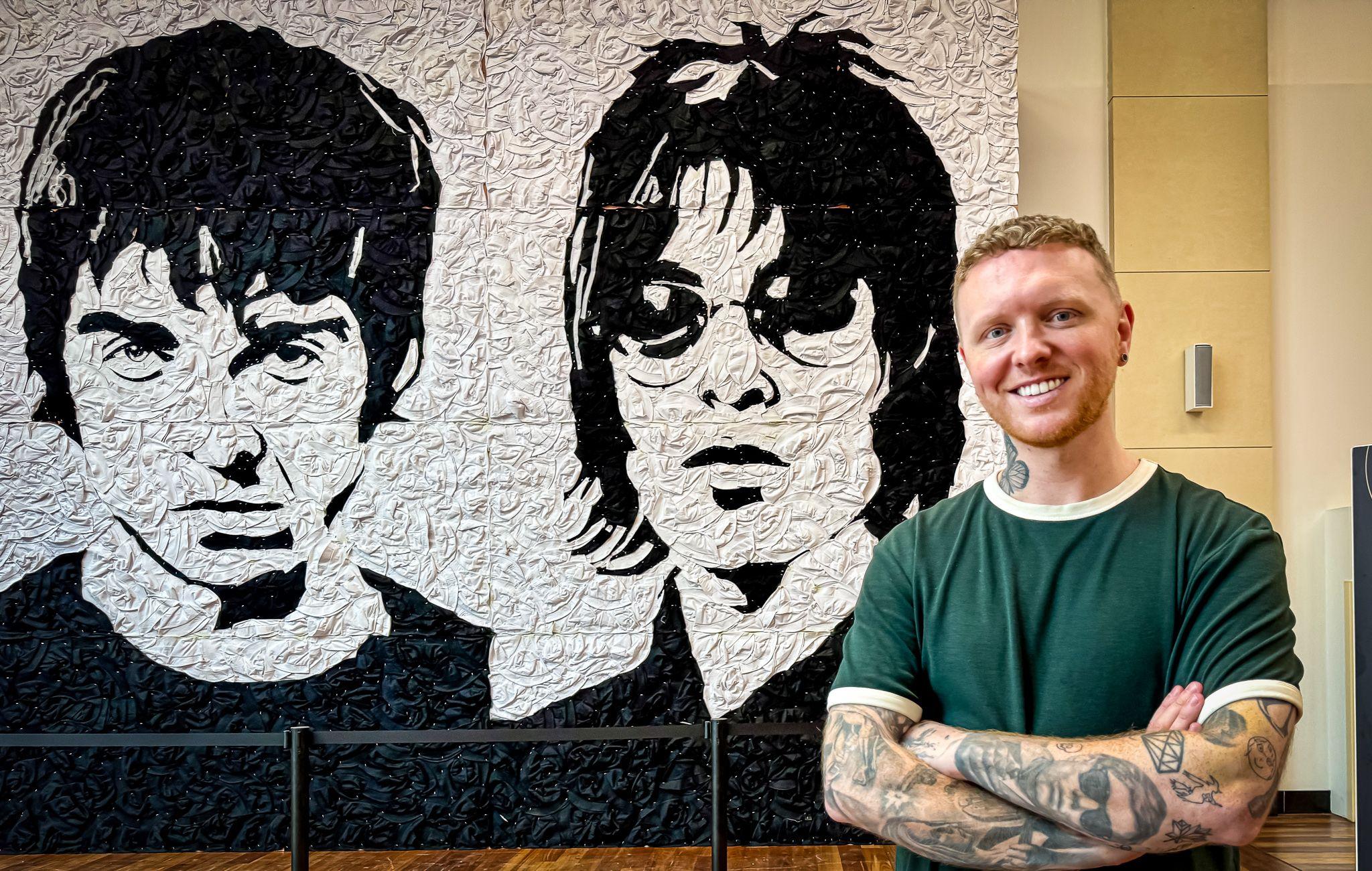 Wyburn standing in front of the mural with his arms crossed. 
