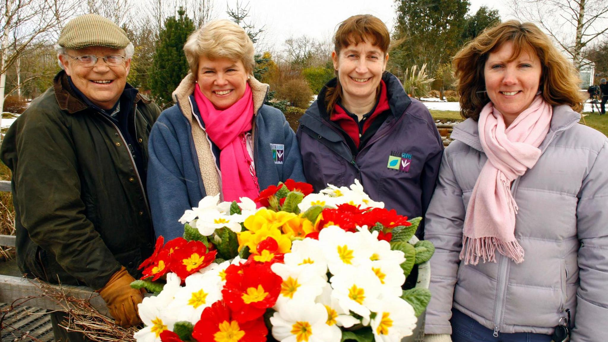 Jim McColl on left of photo smiling with three women co-presenters. There is a bouquet of white and red flowers in front of them