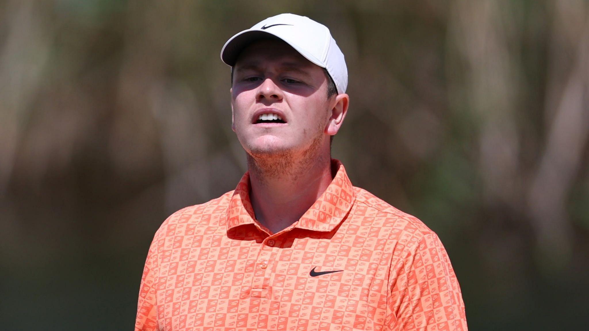 Close up of Bob MacIntyre with his cap casting a shadow over his face as he watches a putt go towards the hole