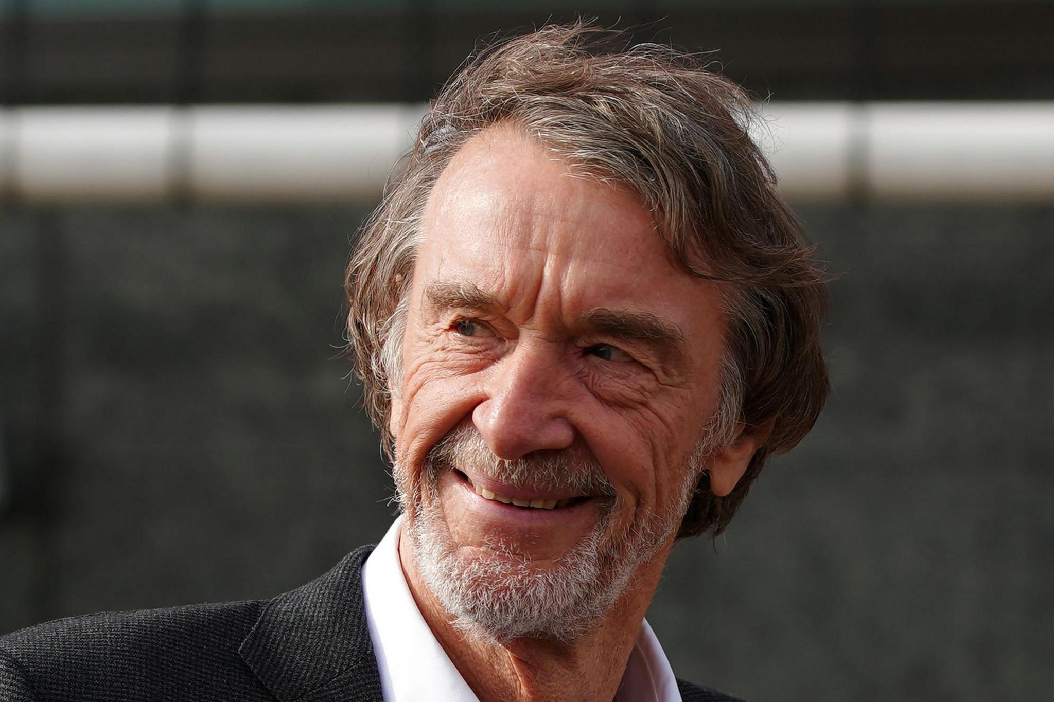 Sir Jim Ratcliffe smiling - he has a beard of mostly white hair,  dark hair and is wearing a suit.