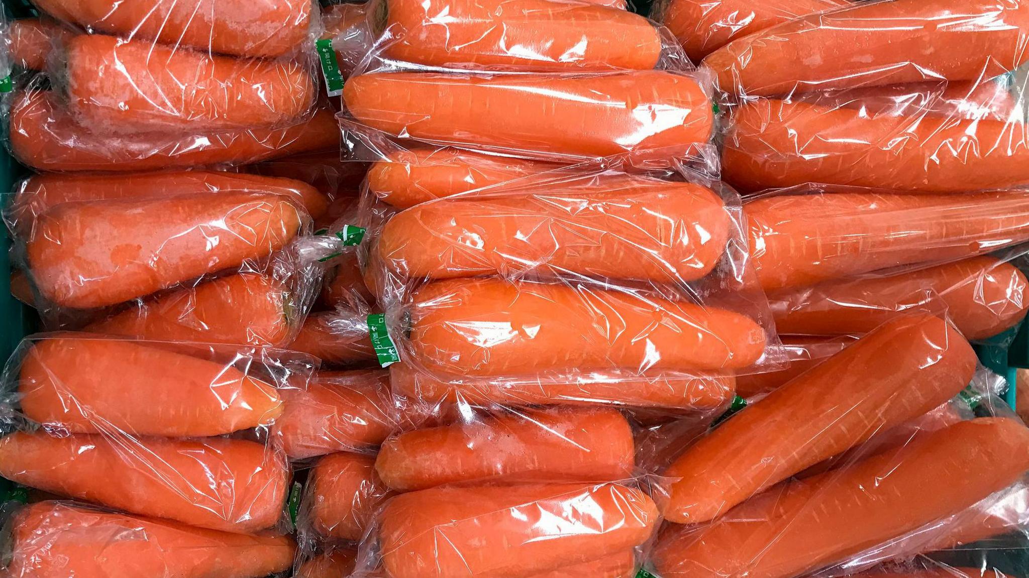 Plastic wrapped carrots in a green grocery box. Stock image