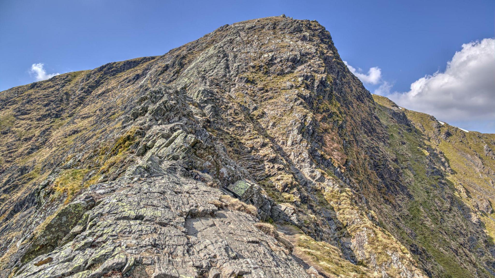 View from Foule Crag of Sharp Edge on Blencathra on a clear sunny day. It a steep, rocky terrain rising to a pointed peak. 