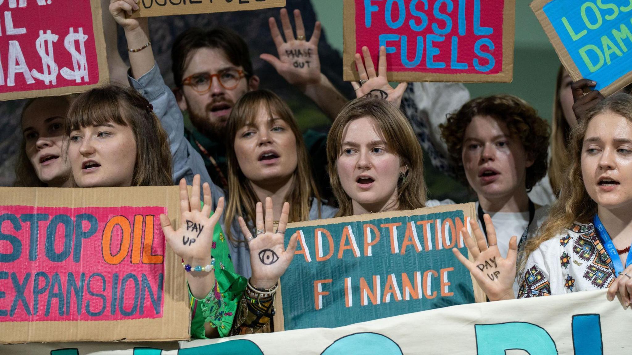 Protesters hold up signs saying "fossil fuels" and "adaptation finance" at the Cop summit 