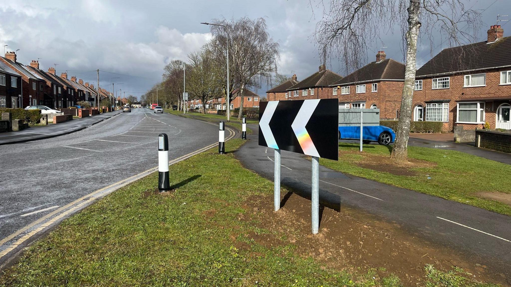 View of the junction road layout showing newly installed bollards and road signs on road bend. A number of houses can be seen in the background