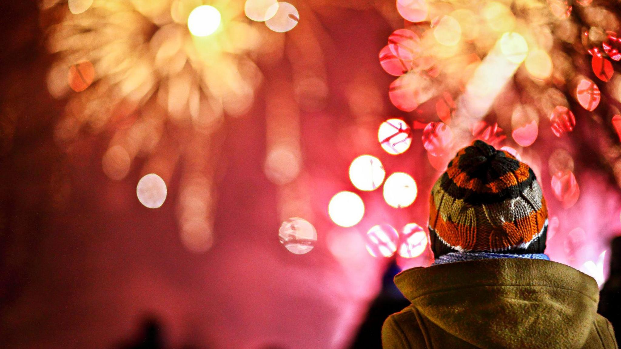 A child wearing a woolly hat and winter coat watching fireworks