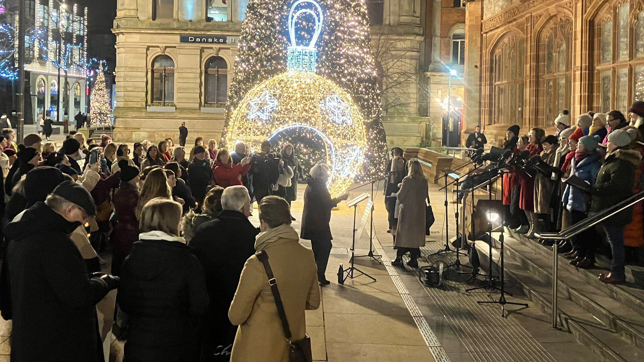 A choir performing in front of the crowd at Guildhall Square. 
A Christmas tree and decorations can be seen in the background.