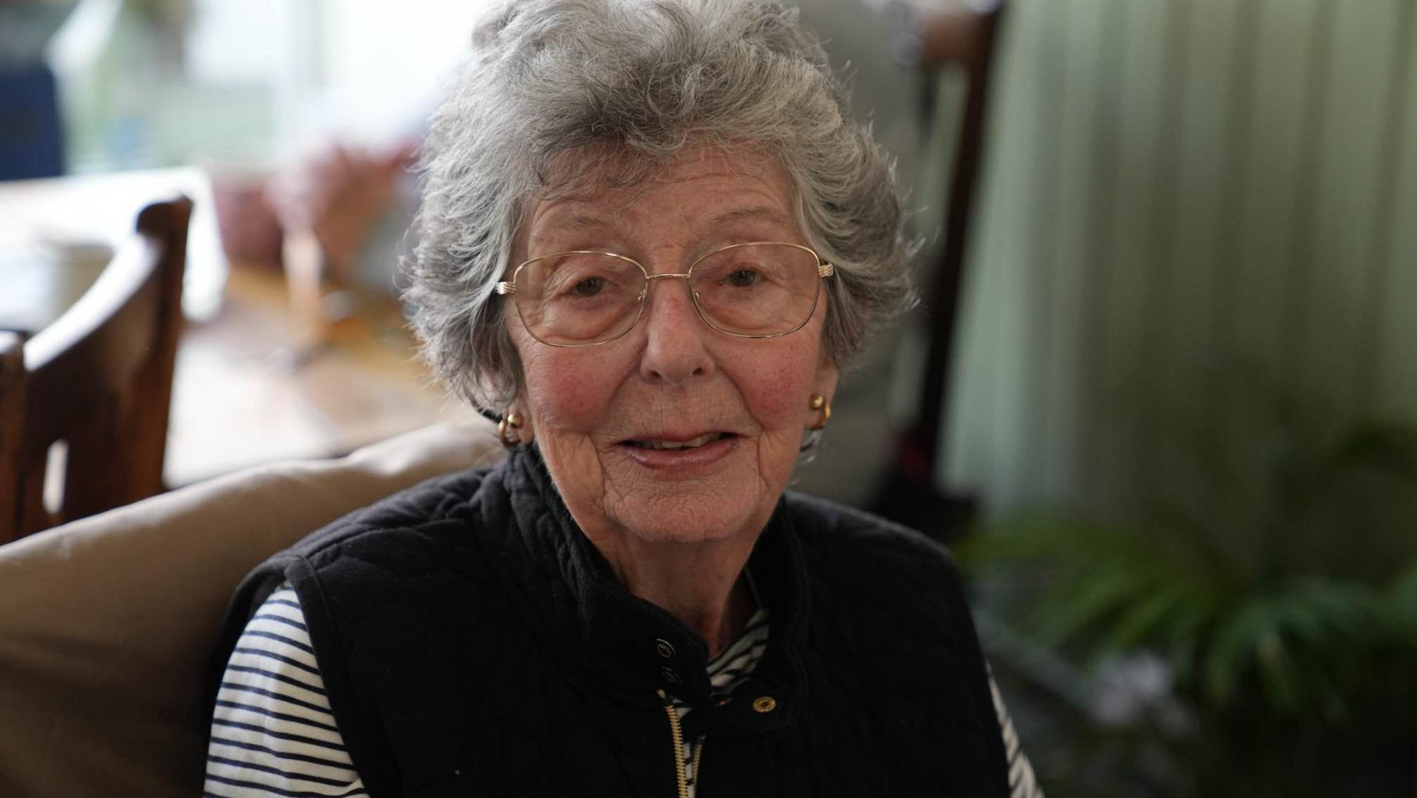 Jan Green wearing a Gillet over a striped top and glasses smiling into the camera 