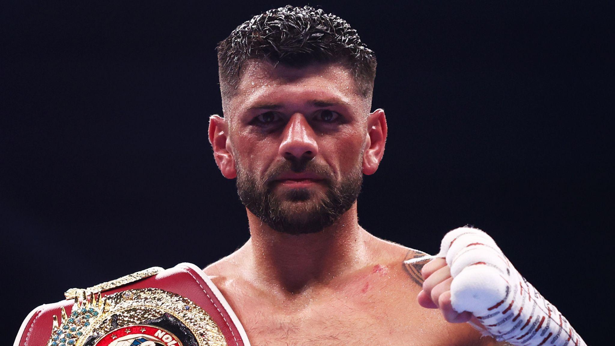 Joe Cordina poses with bandaged left fist raised and boxing belt over right shoulder