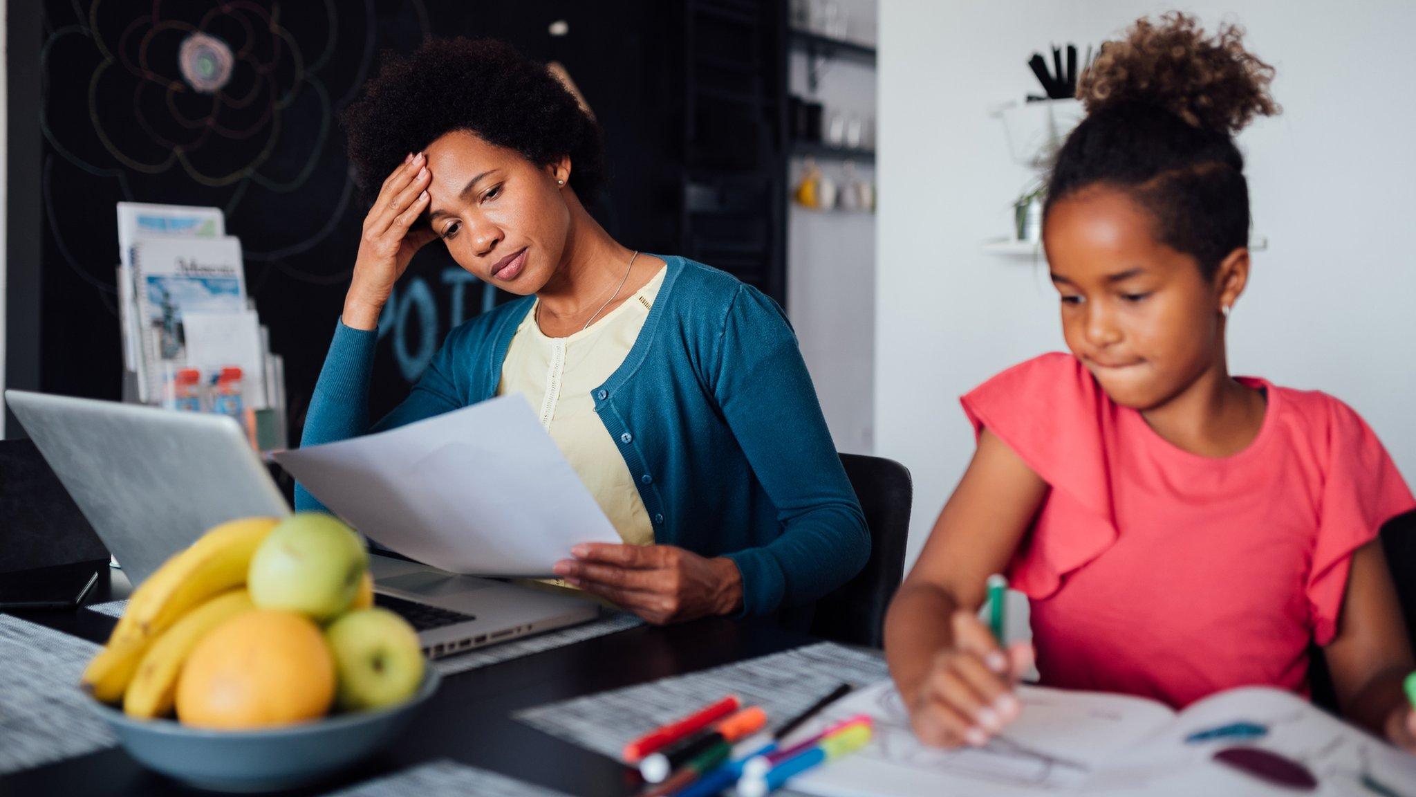 A woman sitting beside her daughter looks at paperwork in front of her laptop