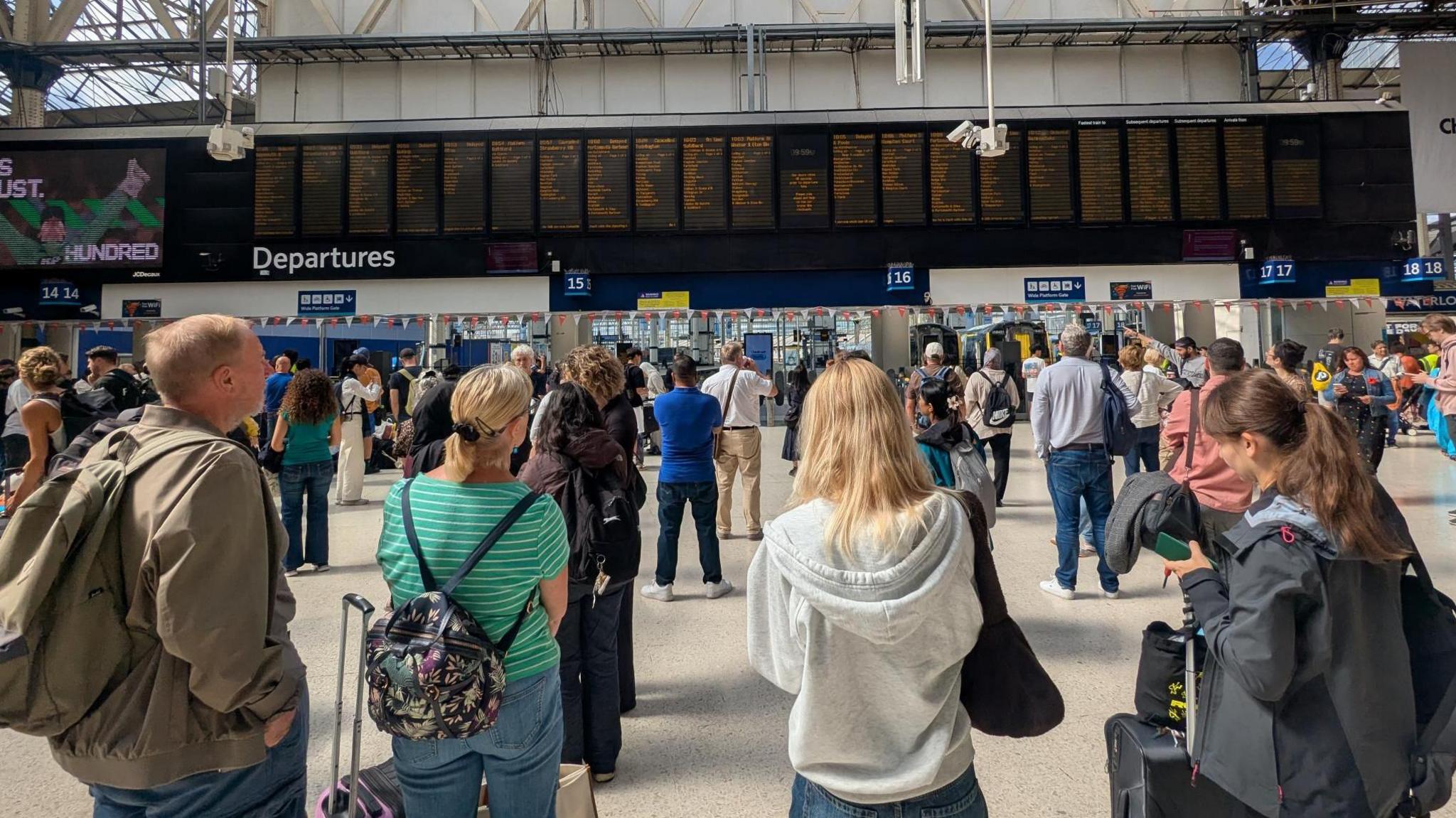 People standing in the concourse of Waterloo station looking at departure boards