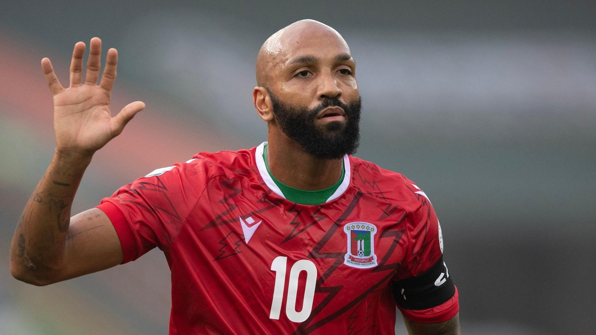 Emilio Nsue, wearing a red Equatorial Guinea shirt, holds up his right palm during a football match