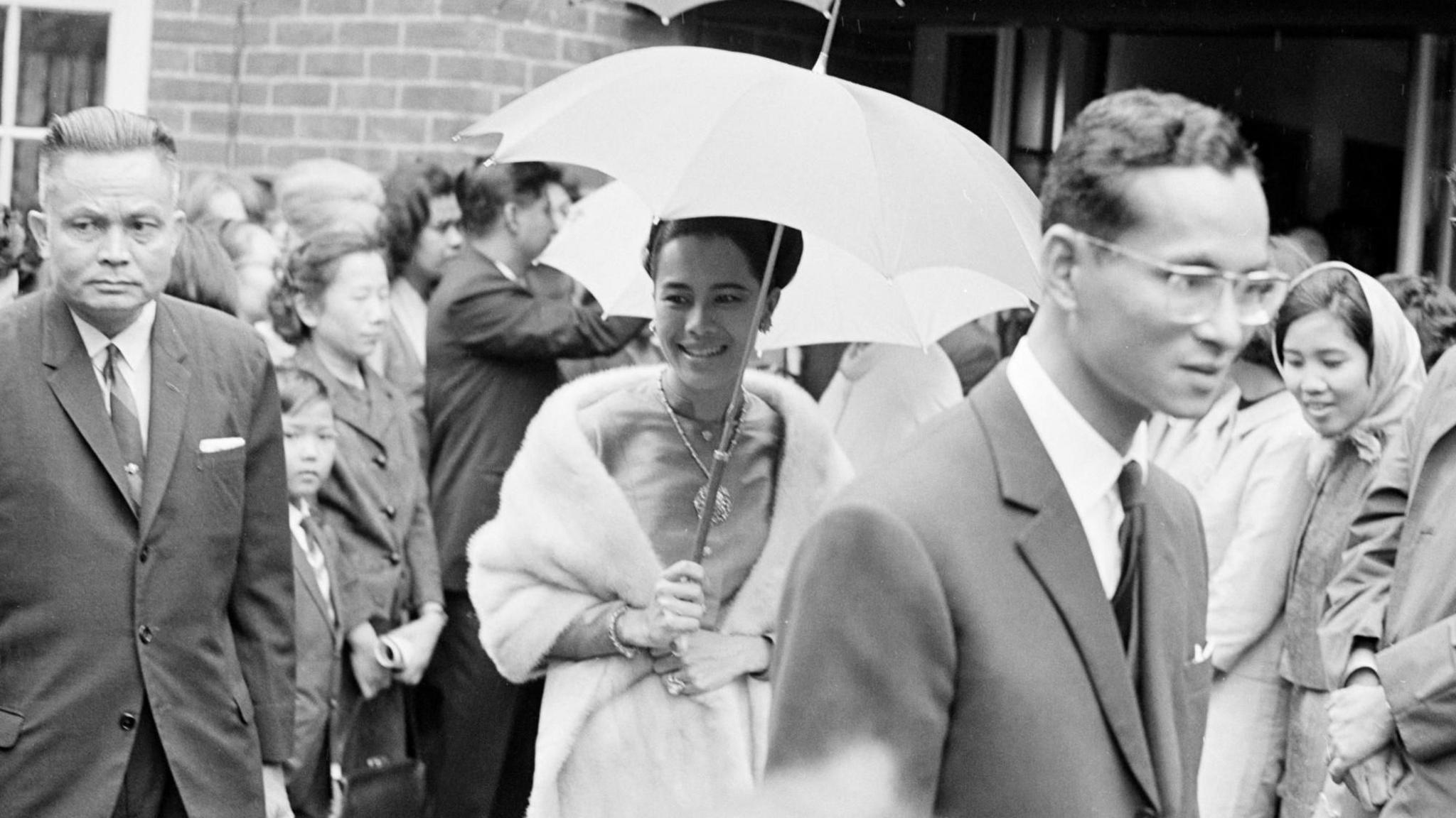 Queen Sirikit holds an umbrella in a black and white photograph.