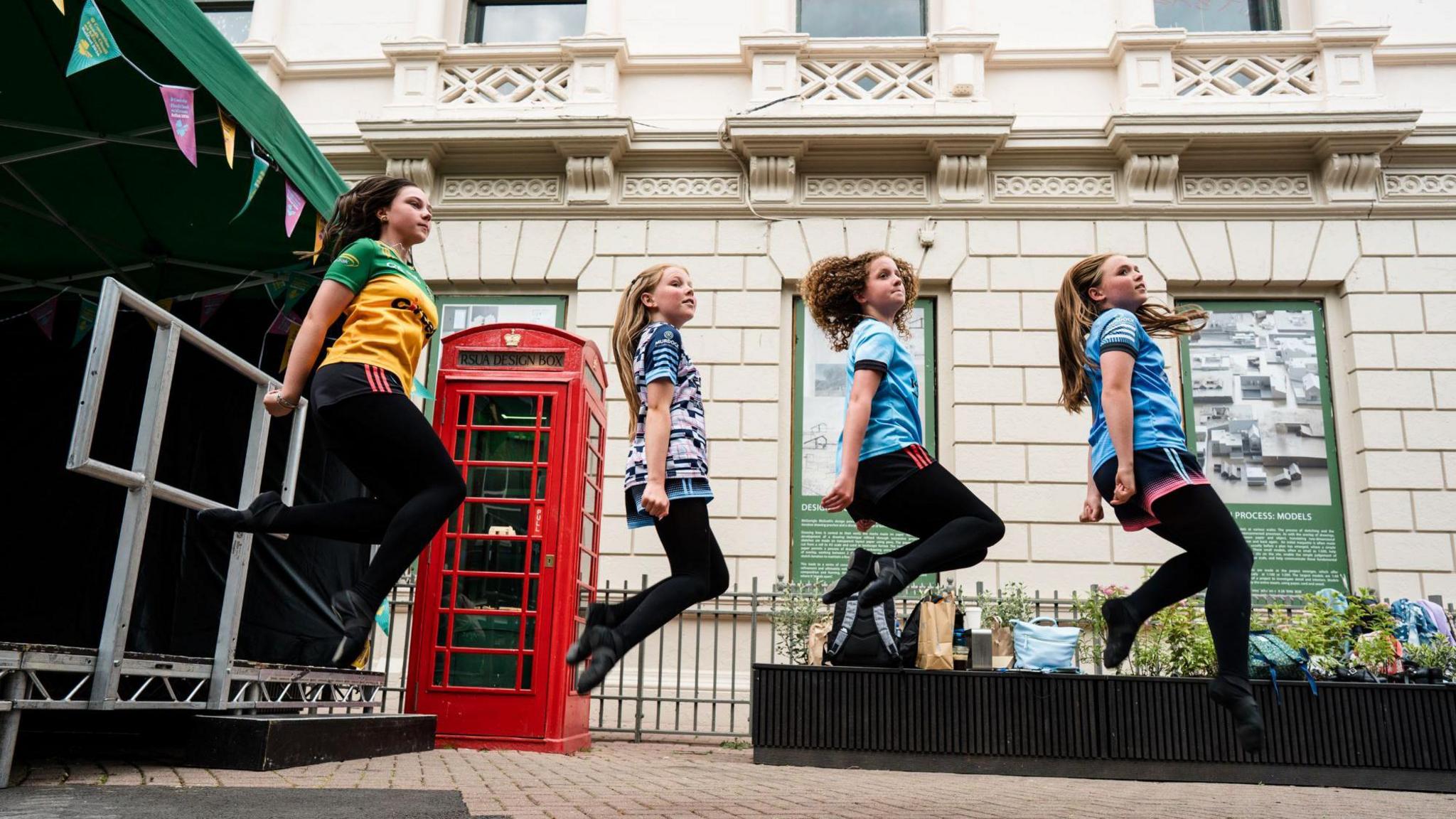 Four young girls Irish dancing. They are all jumping in the air.