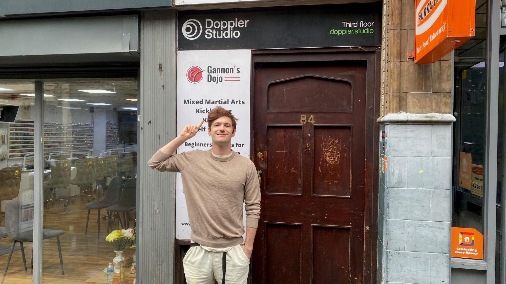 Mr Ferris stood in front of a red door with a sign to the venue above the door. 
