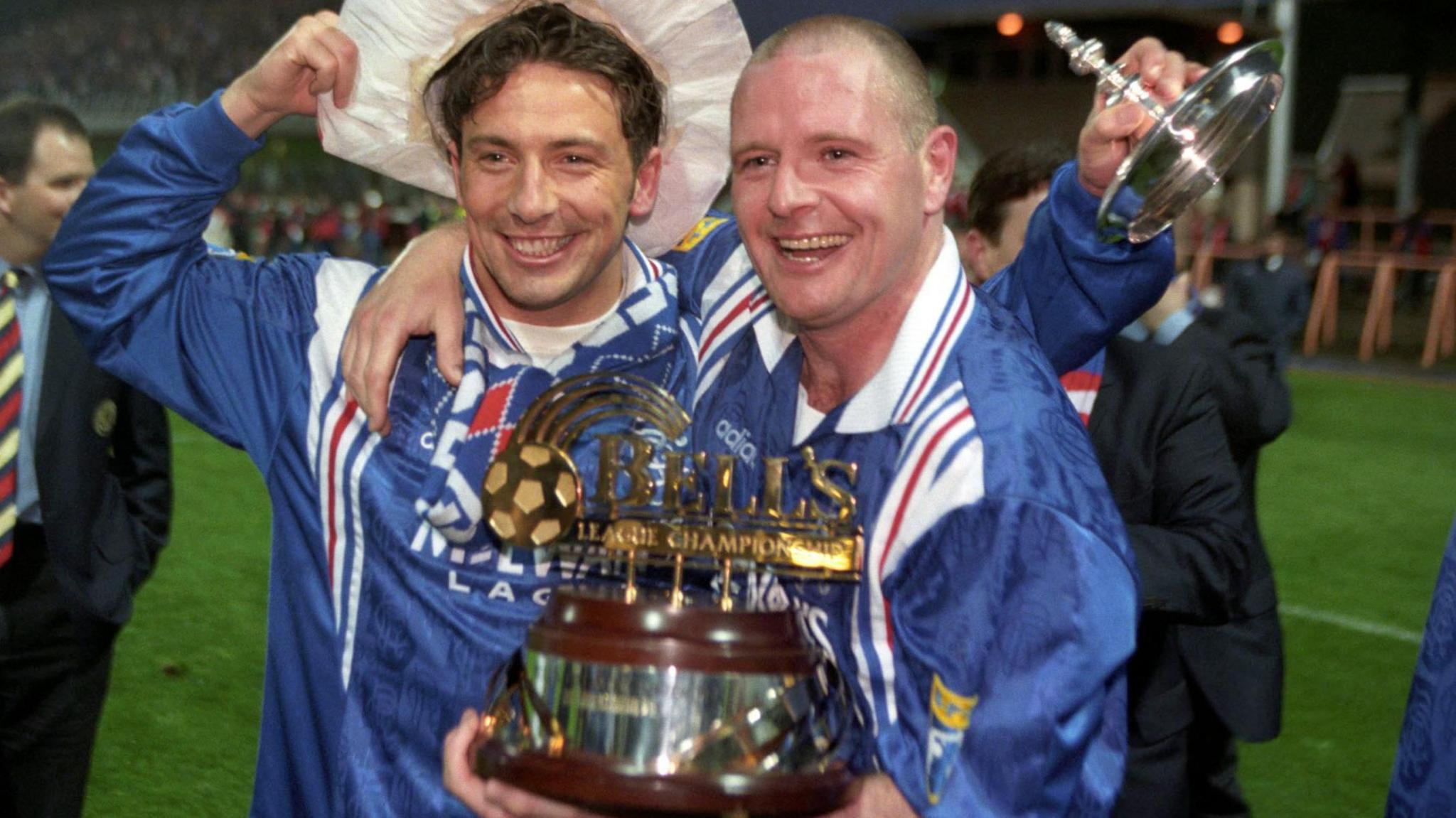 Derek McInnes and Paul Gascoigne wearing blue Rangers shirts hold the trophy and smile towards the camera.