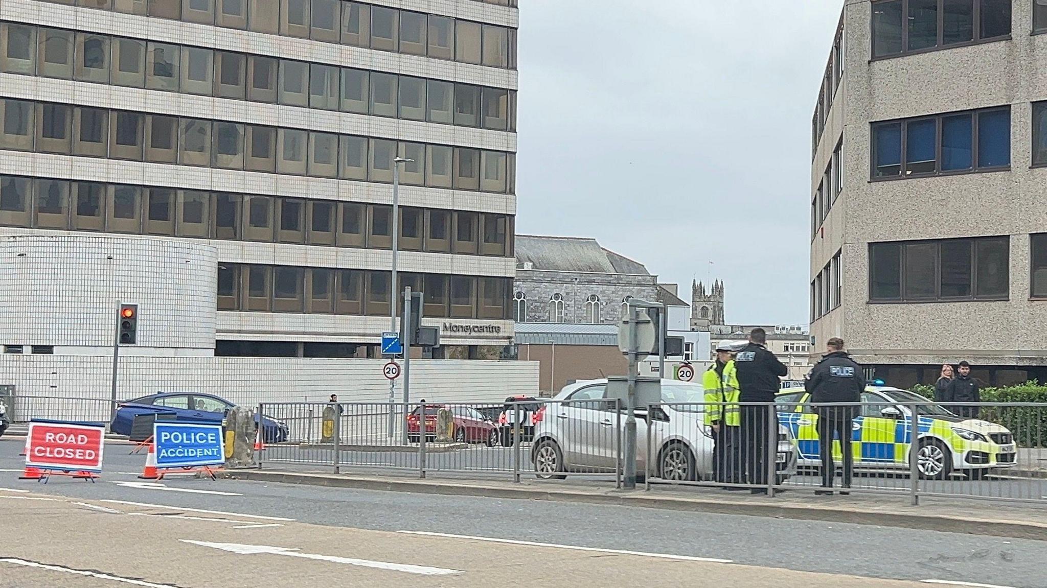A picture from the scene at Cobourg Street. There is police in attendance with signs on the road saying road closed. There is 3 police officers stood together.