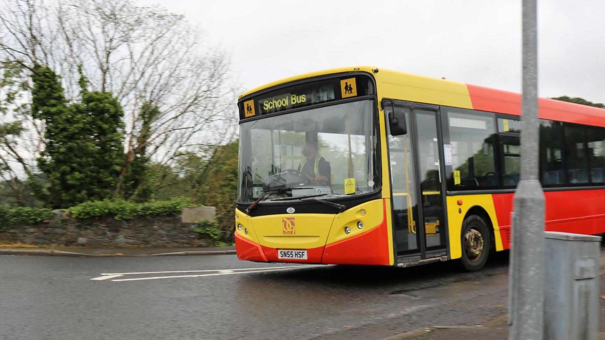 A school bus in Dumfries and Galloway with bright yellow and red livery on a road through a rural area