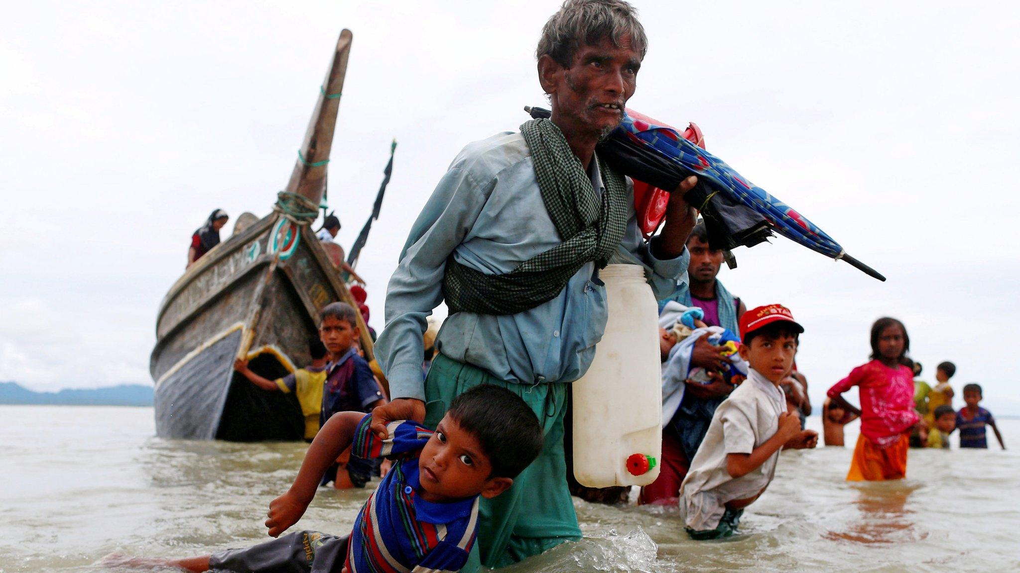 A Rohingya refugee man pulls a child as they walk to the shore after crossing the Bangladesh-Myanmar border by boat through the Bay of Bengal in Shah Porir Dwip, Bangladesh, 10 September 2017