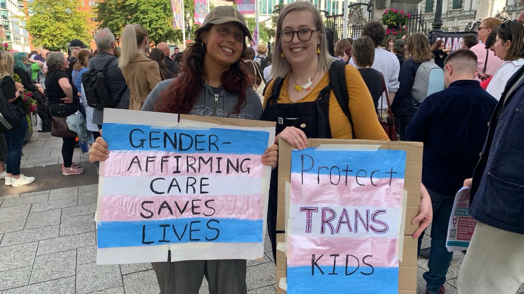 Evangelia and Abigail holding signs that read "gender affirming care saves lives" and "protect trans kids".