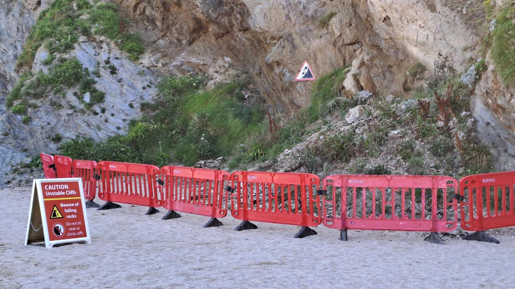 Cordon in place where a cliff rock fall has occurred in Cornwall, involving a number of waist-high plastic barriers and a separate warning sign