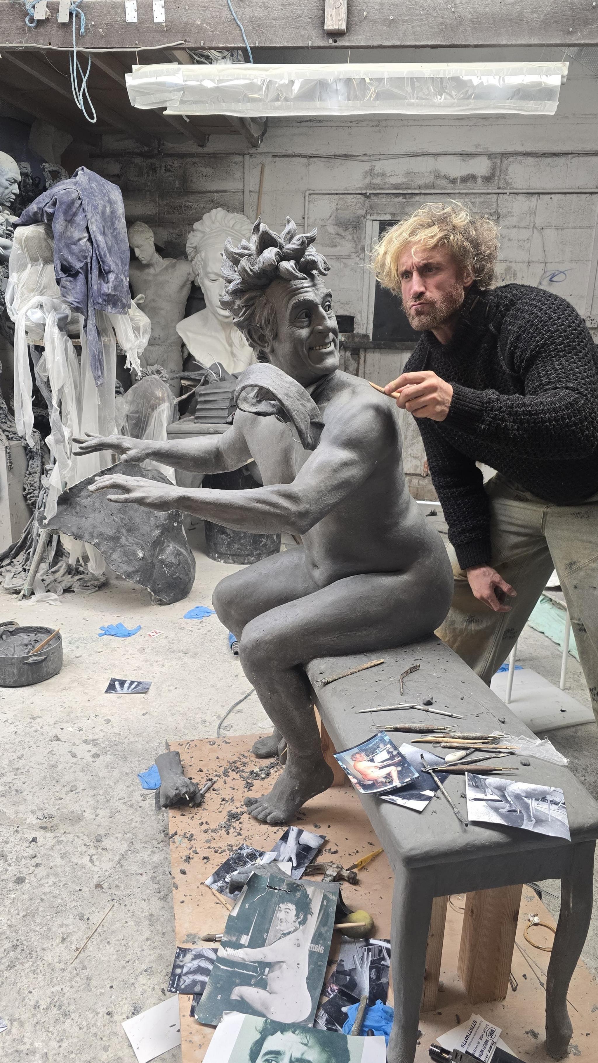 Sculptor Nick Elphick works on the design for the Terry Jones statue in his workshop, crouched over the figure on a bench