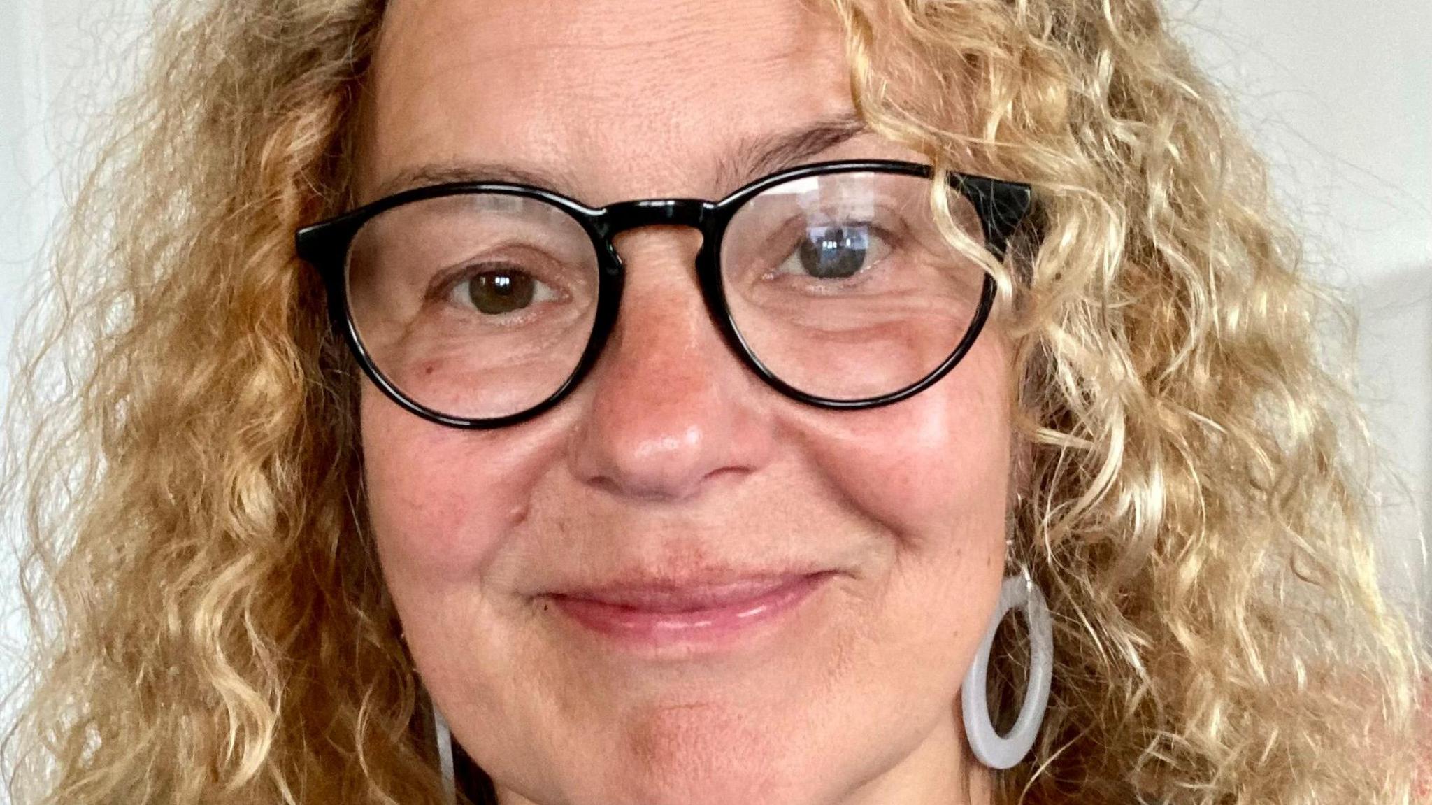 Helen with curly blond hair and black rimmed glasses smiling at the camera.