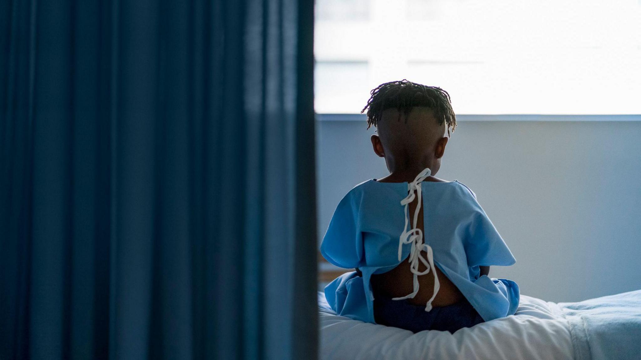 A boy sits in hospital wearing a gown