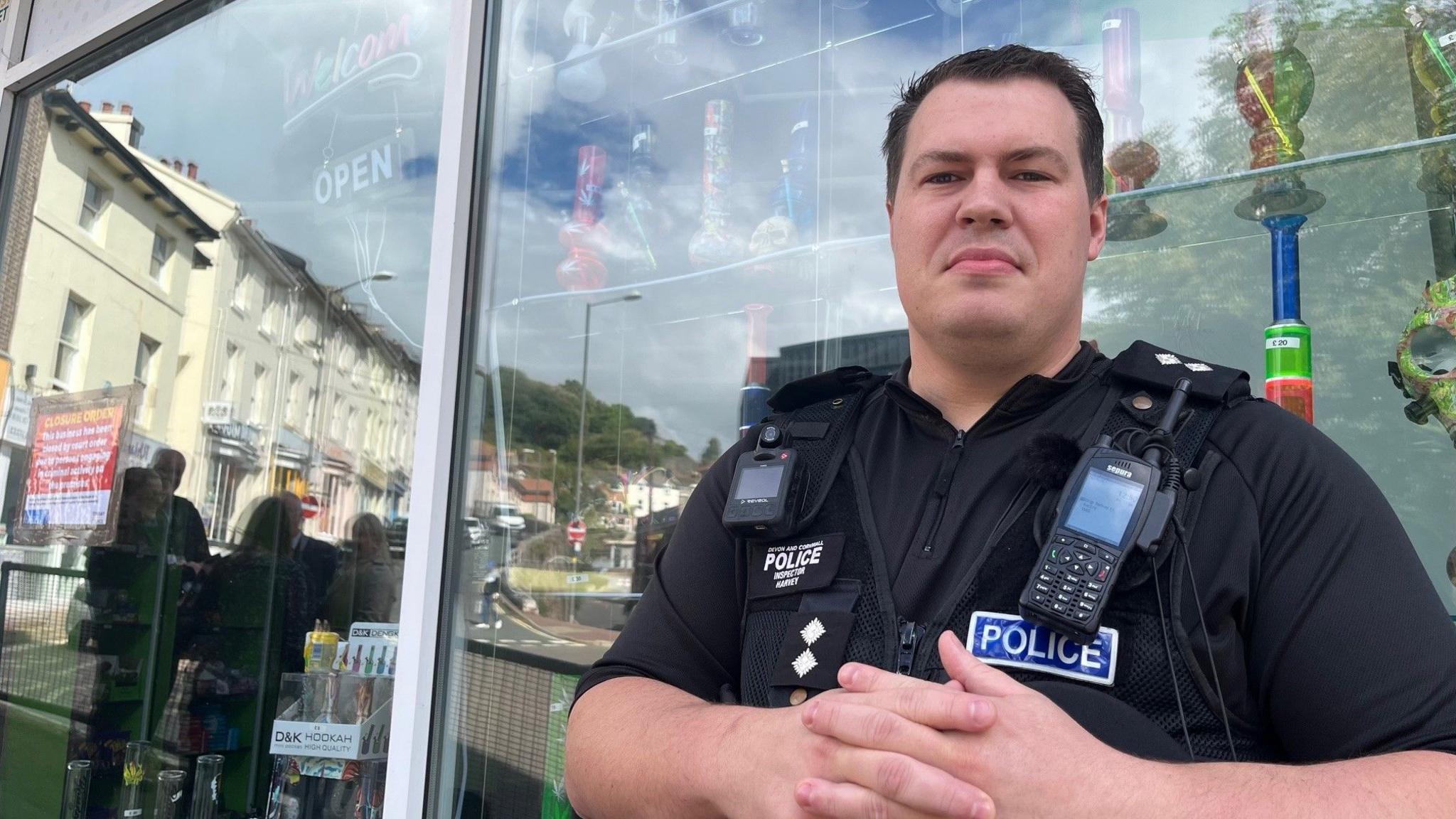 A policeman stands next to a shop window, with a closure sign attached to it.