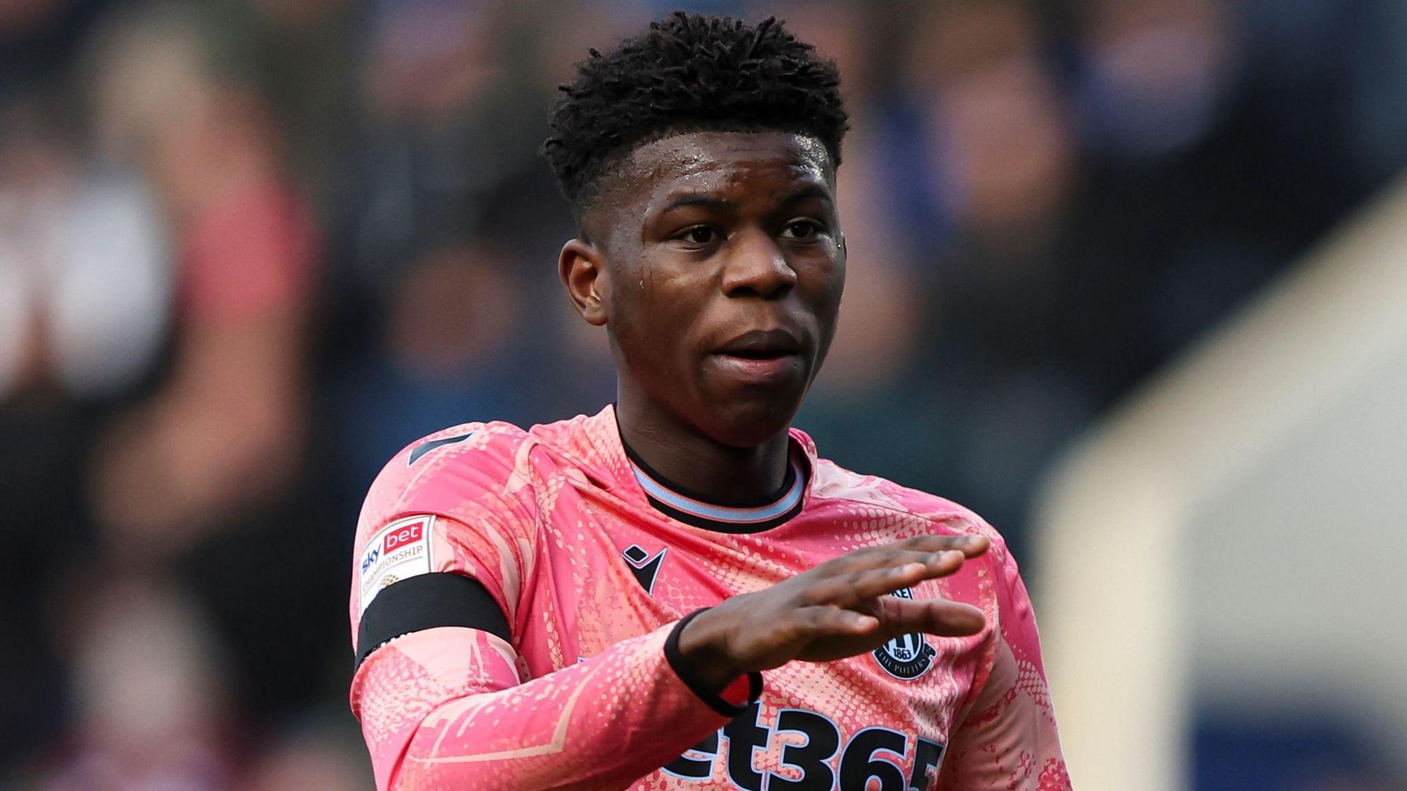 Stoke City's Sol Sidibe is wearing the club's pink away kit and is stretching out his right hand during a stoppage in play
