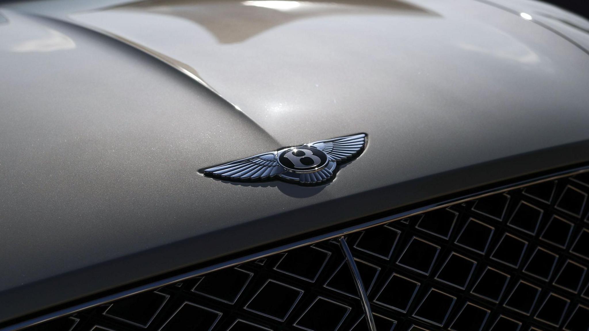 The Bentley logo on the front of a grey car, just above the radiator grill. The badge is a central "B" with wings either side.