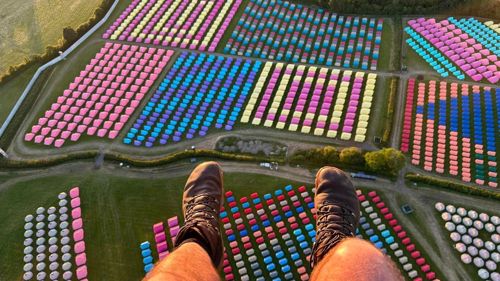 Aerial view of Worthy Farm. The paraglider's legs can be seen at the bottom of the frame, and fields are lined with colourful tents