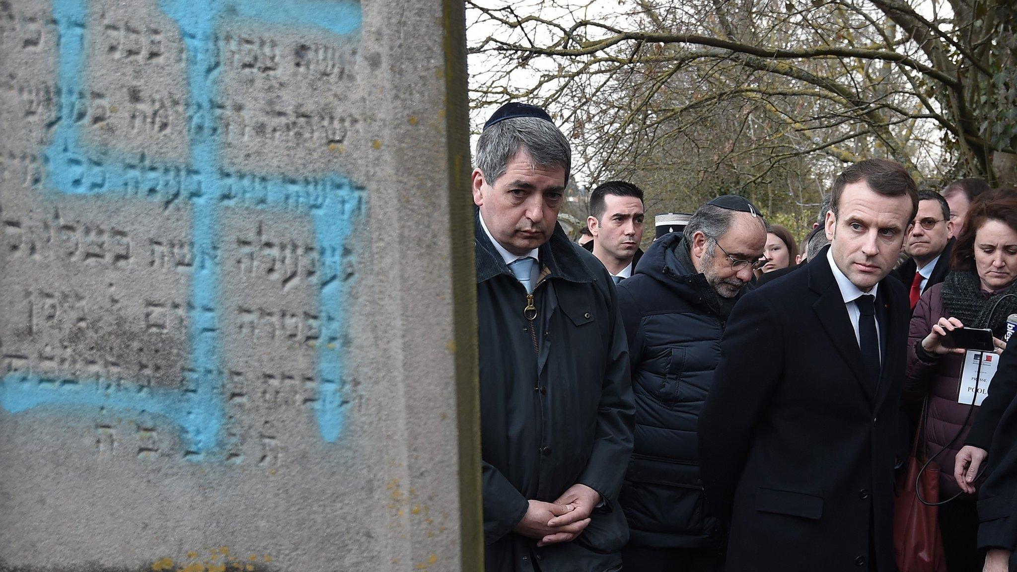 French President Emmanuel Macron looks at a grave vandalised with a swastika during a visit at the Jewish cemetery in Quatzenheim, France, 19 February 2019,