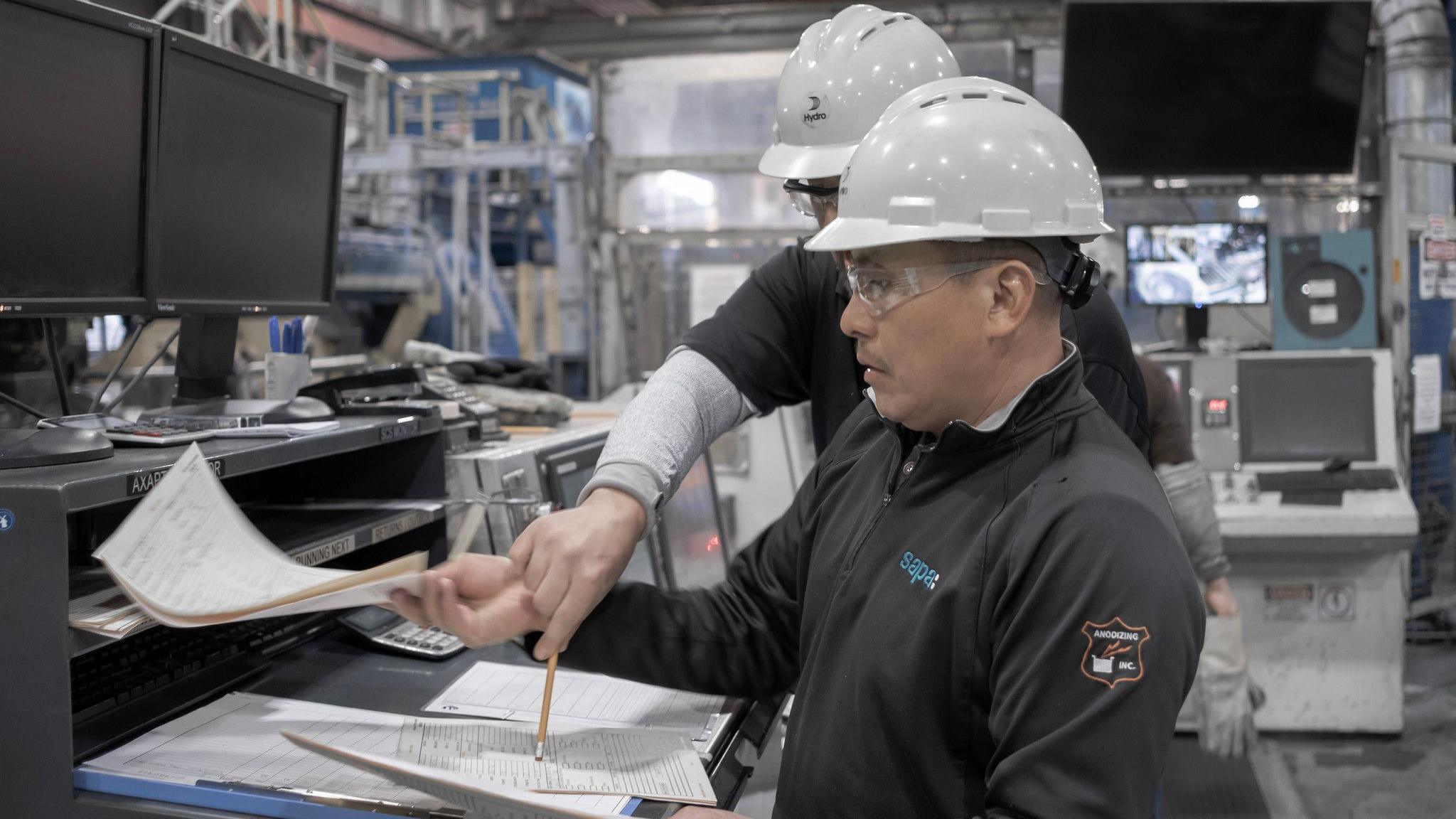 Appearing confused two factory staff look at paperwork at a Norsk Hydro plant