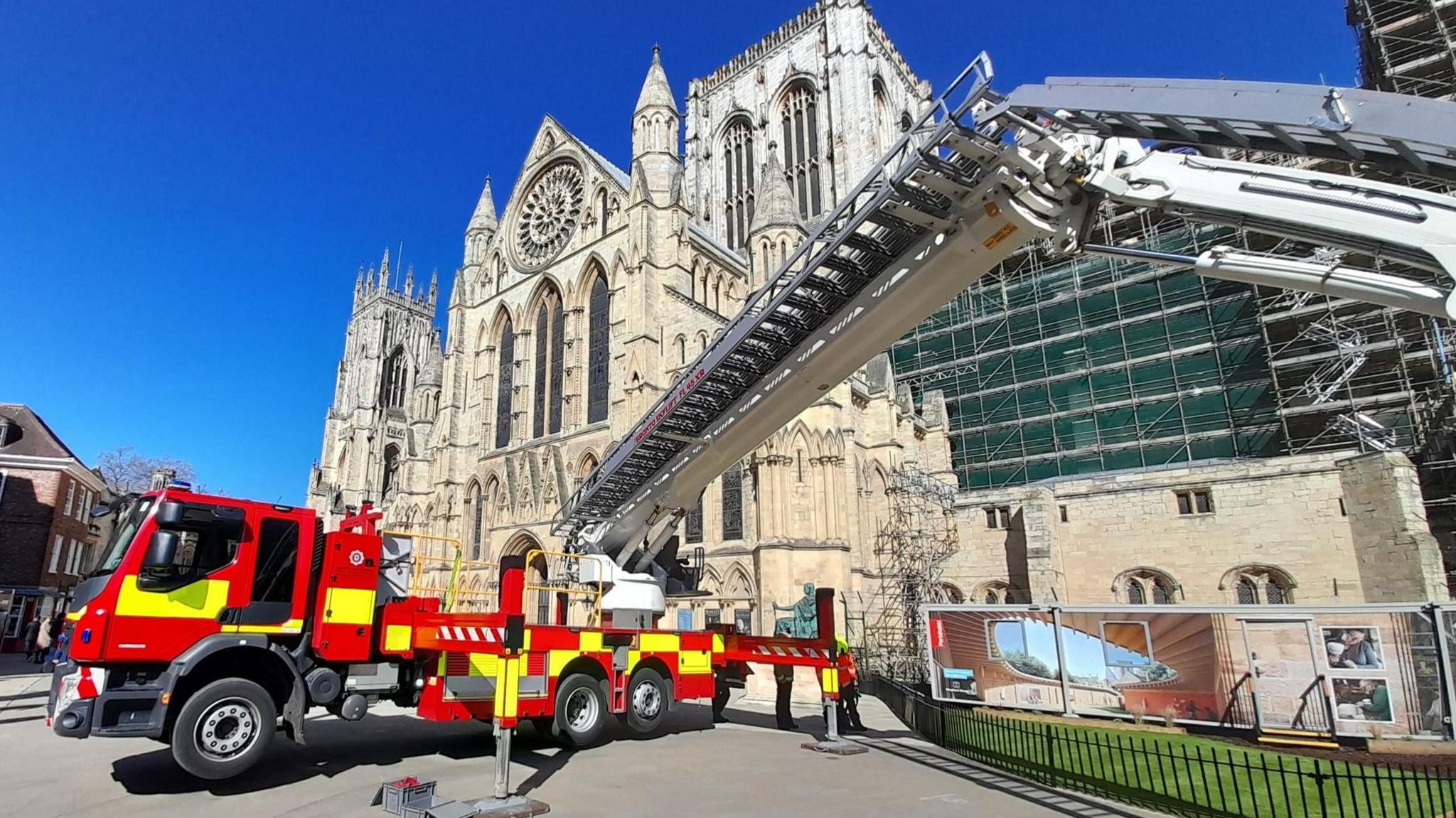 A fire engine with an aerial platform is stationed outside York Minster on a sunny day.
