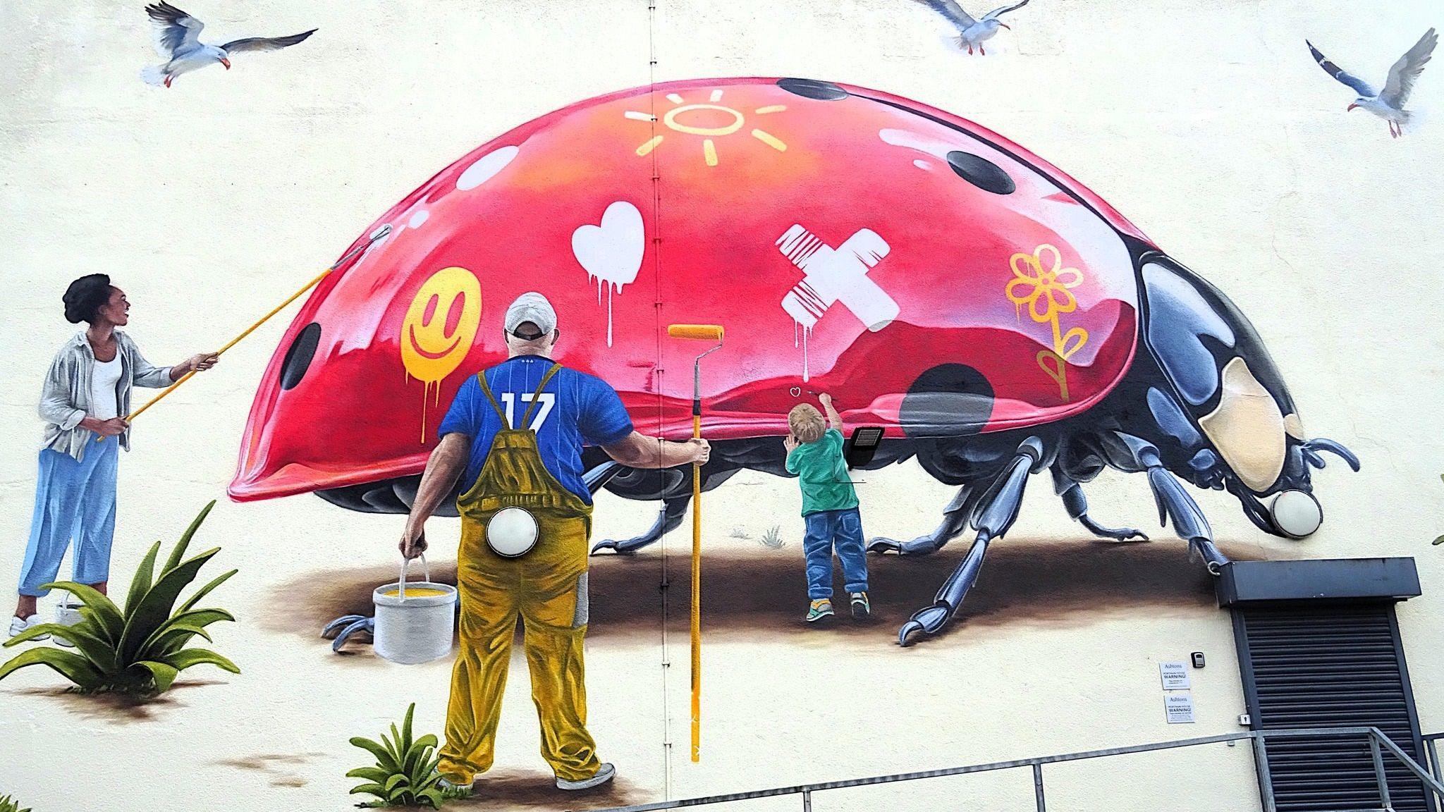 One of the large-scale murals that has already been painted in Ipswich by London-based artist Woskerski. It depicts a ladybird that is missing some of its black spots which members of the community are painting on to it showing community spirit.