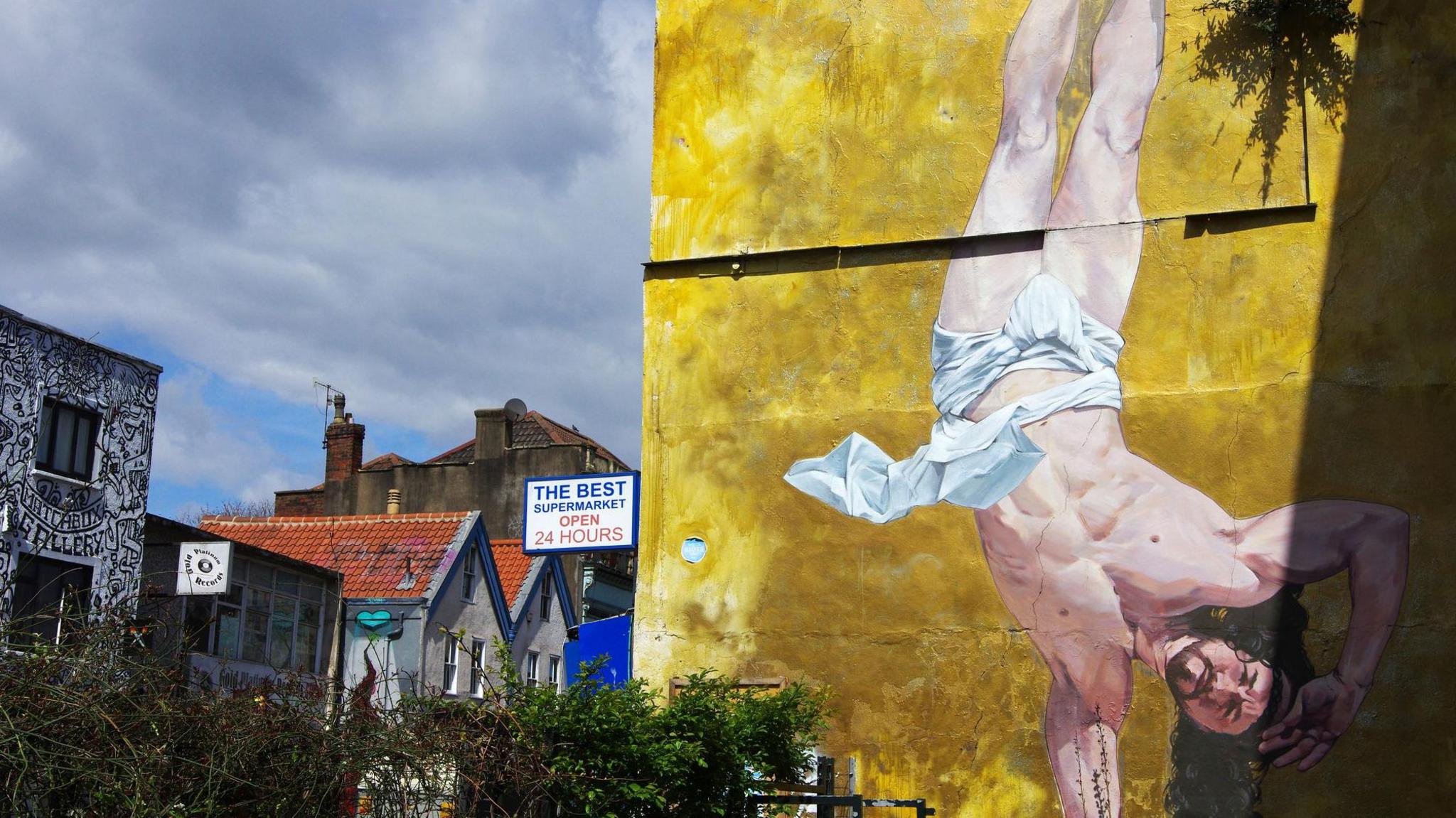 A large mural on the side of a building in Stokes Croft of Jesus breakdancing with a rich gold background. The rest of stokes croft can be seen to the side in the background.
