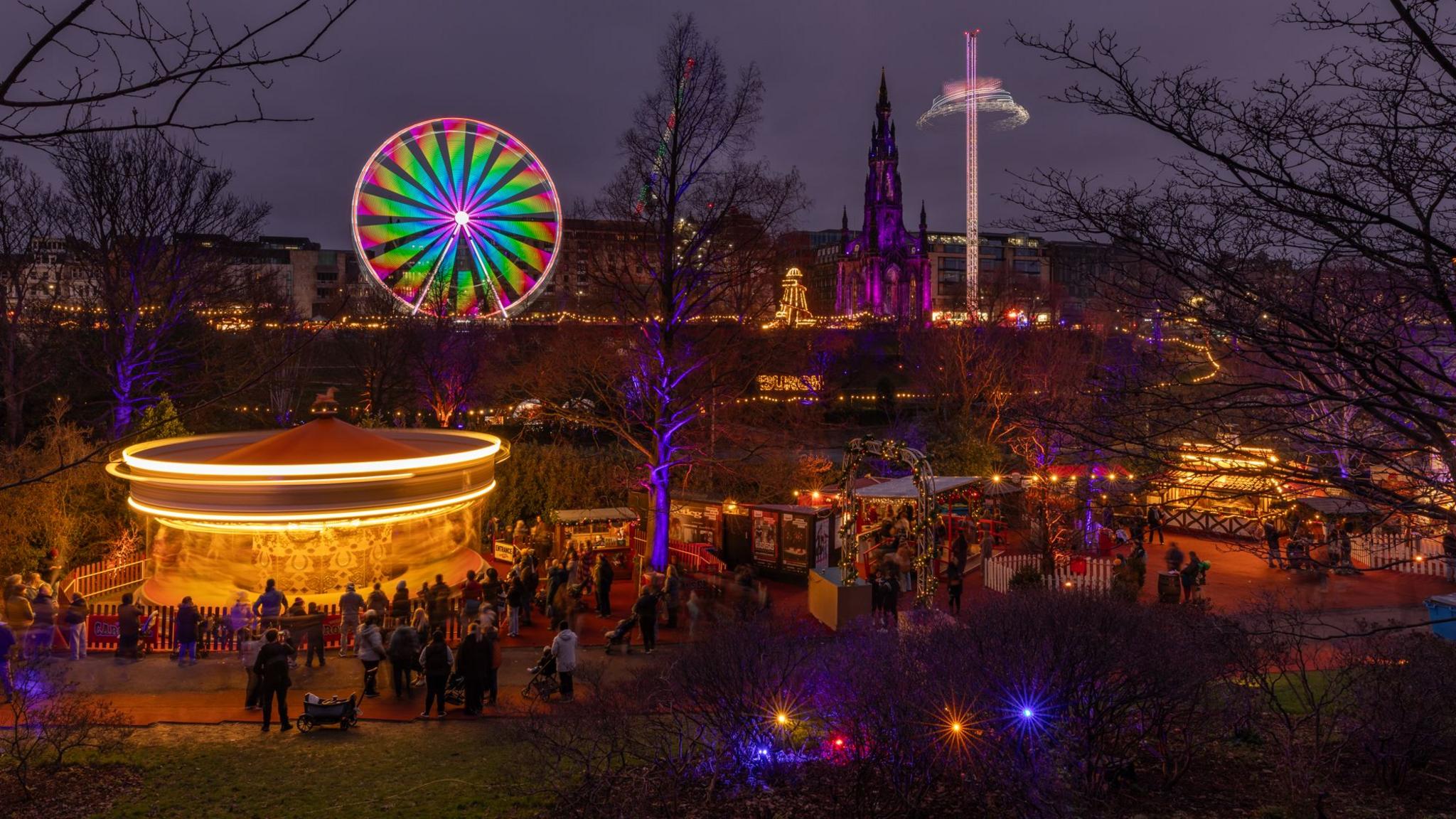 Edinburgh's Christmas market, with stalls, a carousel lit up in yellow and a big wheel in the distance with green and red lights.
