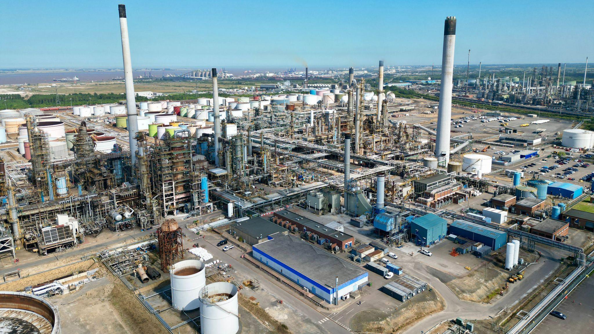 A drone view of the Prax Lindsey Oil Refinery. A cluster of metal structures rising to the blue sky.
