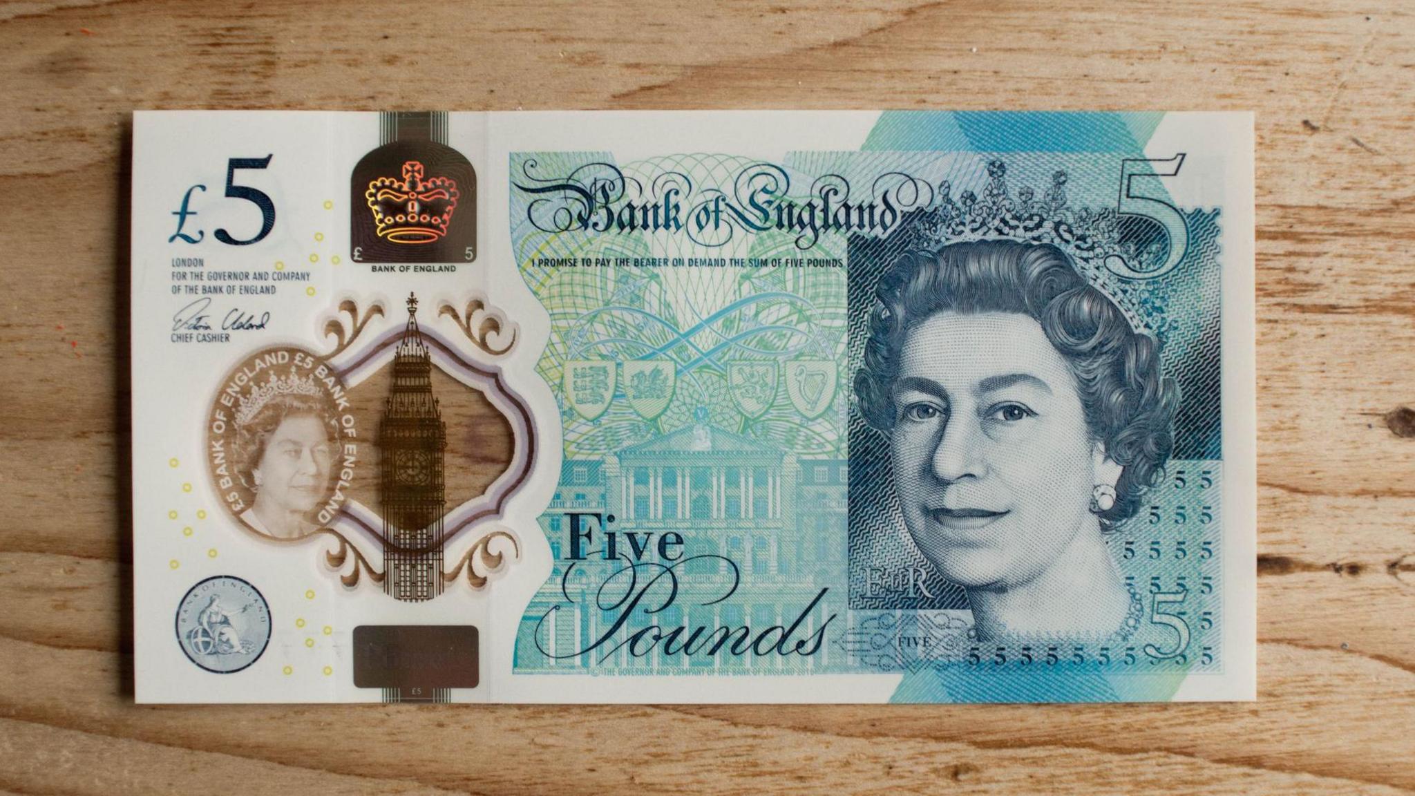 New five pound note on a wooden kitchen table background with Queen's head visible