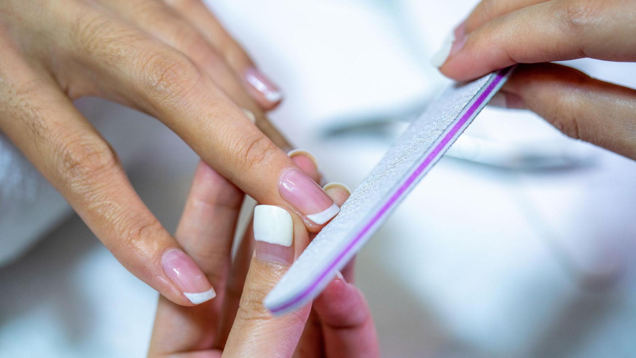Closeup shot of a woman in a nail salon receiving a manicure by a beautician with nail file.