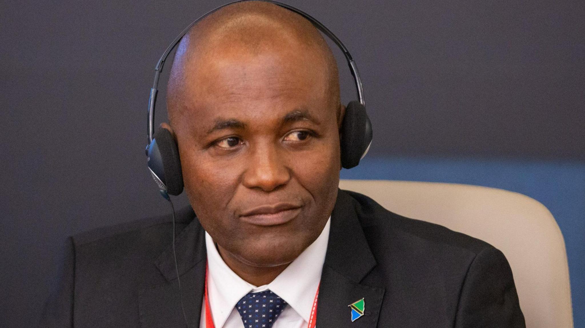 Faustine Ndugulile in a black suit and headphones and a Tanzanian flag lapel